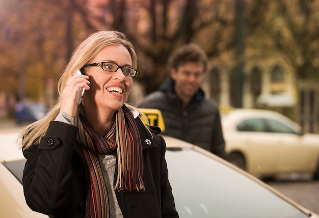 Jeune femme devant un taxi avec téléphone