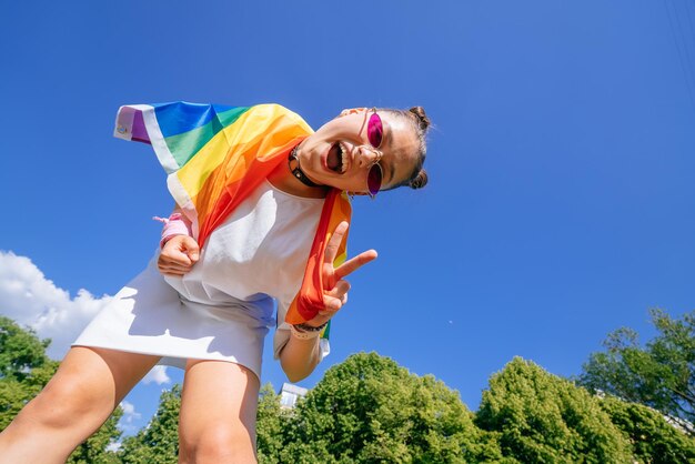 Une jeune femme développe un drapeau arc-en-ciel contre le ciel