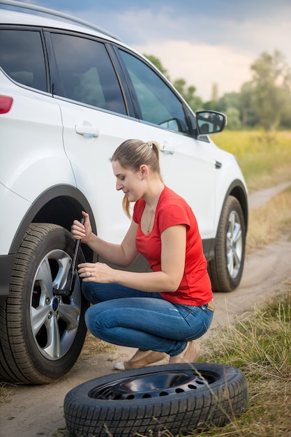Photo jeune femme dévissant les écrous sur la roue plate de la voiture sur le terrain