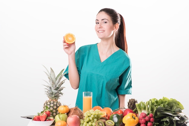 Jeune femme diététiste assise au bureau et montrant des légumes et des fruits colorés