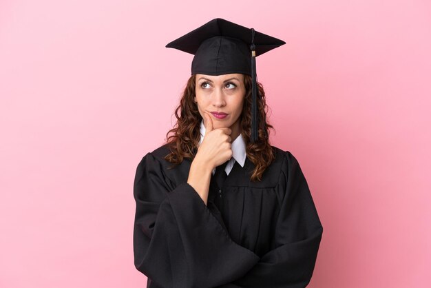 Jeune femme diplômée universitaire isolée sur fond rose ayant des doutes et avec une expression de visage confuse