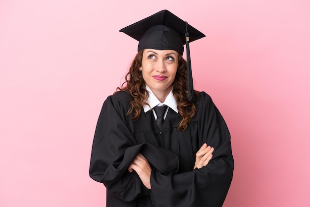 Jeune femme diplômée universitaire isolée sur fond rose faisant un geste de doute tout en levant les épaules