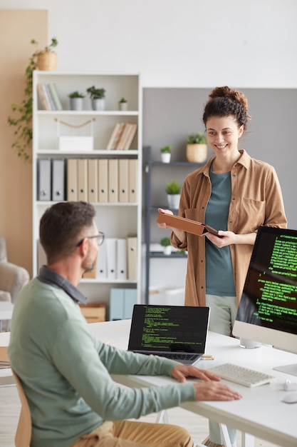 Jeune femme discutant avec son collègue nouveau programme informatique sur ordinateur pendant la journée de travail au bureau