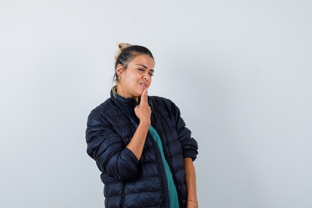 Jeune femme avec les doigts sur le menton en doudoune et à l'air confiant , vue de face.