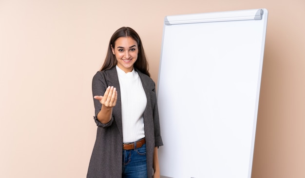 Jeune femme donnant une présentation sur tableau blanc invitant à venir avec la main.