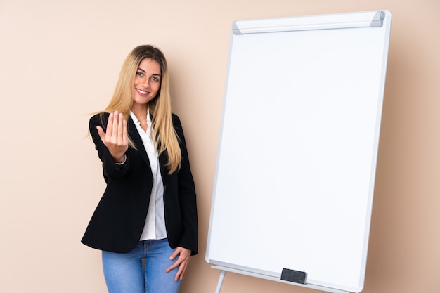 Jeune femme donnant une présentation sur tableau blanc et invitant à venir avec la main