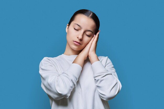 Jeune femme dormant avec les yeux fermés tenant la main près de l'oreille geste de sommeil sur fond bleu studio langage corporel sommeil sain beauté style de vie jeunes étudiants concept