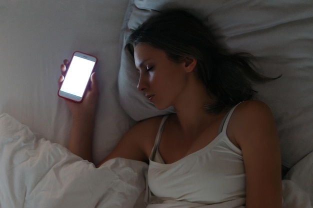 La jeune femme dort avec le smartphone dans sa main. Dépendance aux smartphones et aux réseaux sociaux. Concept de dépendance aux gadgets et à Internet