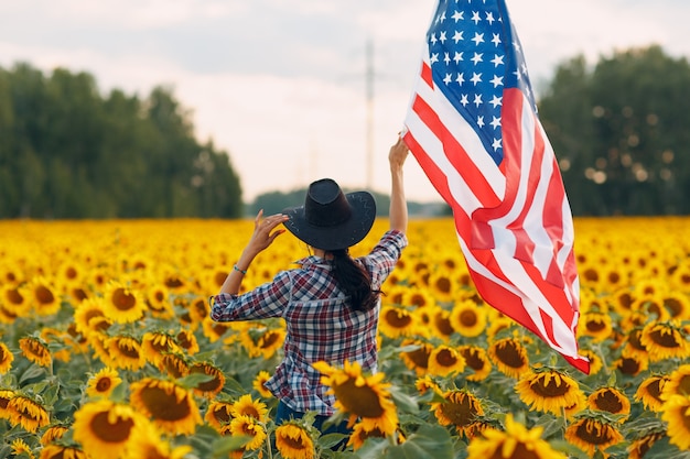 Jeune femme avec drapeau américain dans le champ de tournesol. Concept de la fête de l'indépendance du 4 juillet aux États-Unis.