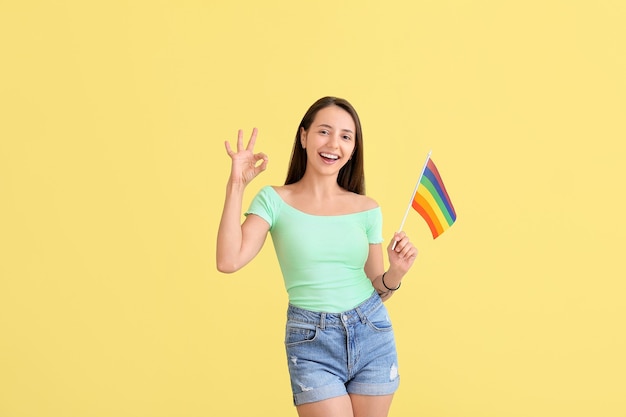 Jeune femme avec drapeau LGBT montrant OK sur jaune