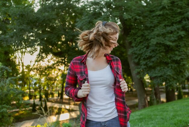 Jeune femme drôle et joyeuse écoute de la musique avec des écouteurs dans le parc au lever du soleil.