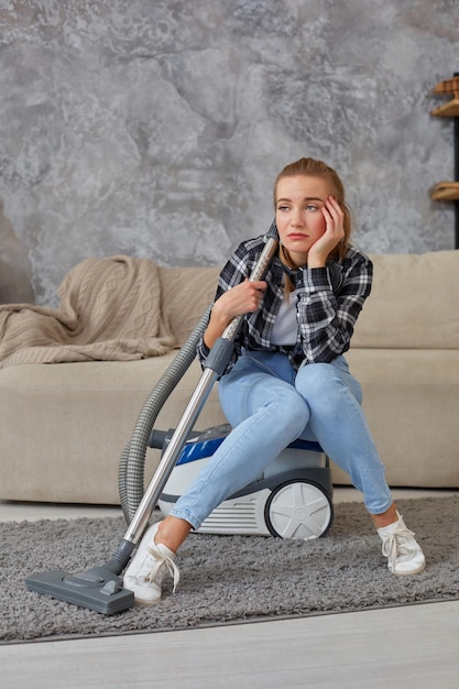 Jeune femme avec du matériel de nettoyage prêt à nettoyer la maison, assise sur un canapé. Concept de service de nettoyage professionnel, espace de copie. Fatigue