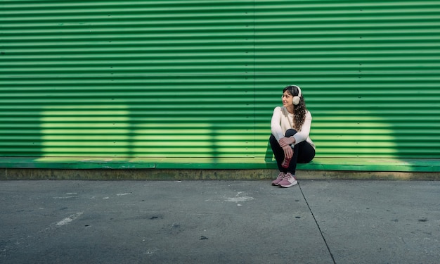 Jeune femme écoutant de la musique appuyé contre un mur vert