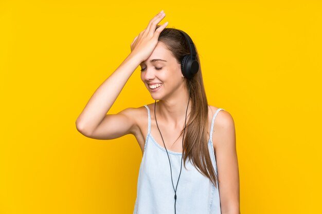 Jeune femme écoutant de la musique sur un mur jaune isolé a réalisé quelque chose et dans l'intention de la solution