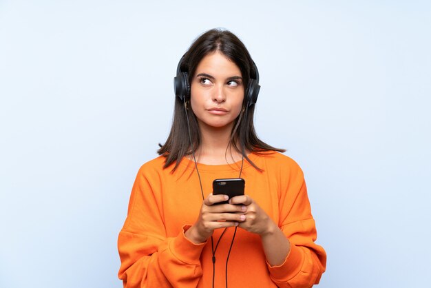 Jeune femme écoutant de la musique avec un téléphone portable sur un mur bleu isolé