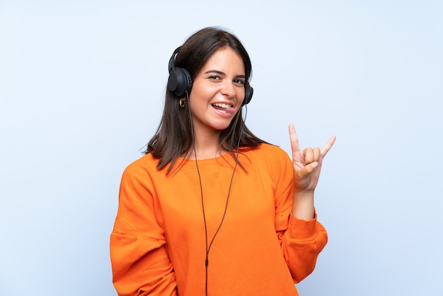 Jeune femme écoutant de la musique avec un téléphone portable sur un mur bleu isolé