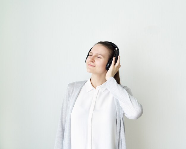 Jeune femme écoute de la musique avec des écouteurs, fille debout devant un mur gris clair