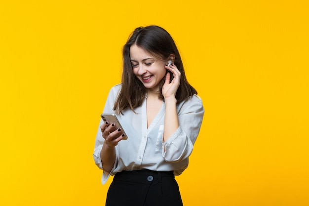 Une jeune femme écoute de la musique sur des écouteurs sans fil sur fond jaune