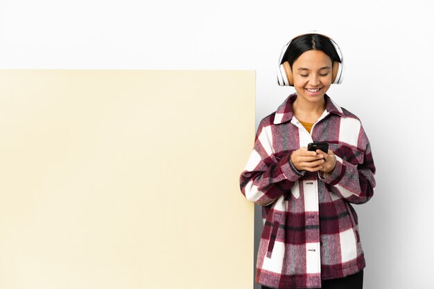 Jeune femme à l'écoute de la musique avec une grande pancarte vide sur fond isolé l'envoi d'un message avec le mobile