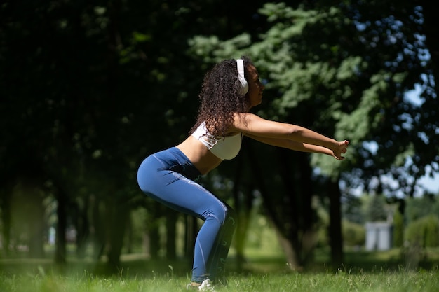 Jeune femme avec des écouteurs effectuant des squats à l'extérieur