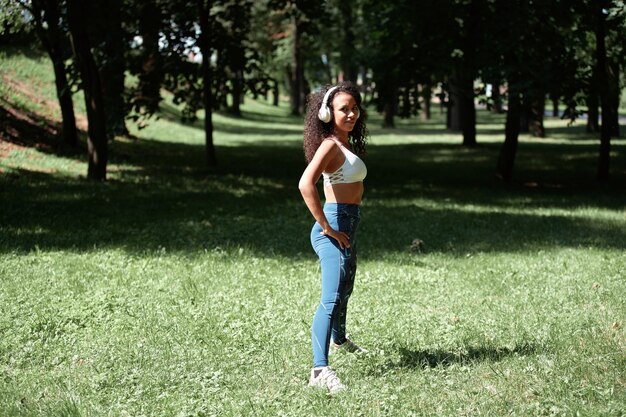 Jeune femme avec des écouteurs fait de la gymnastique dans le parc