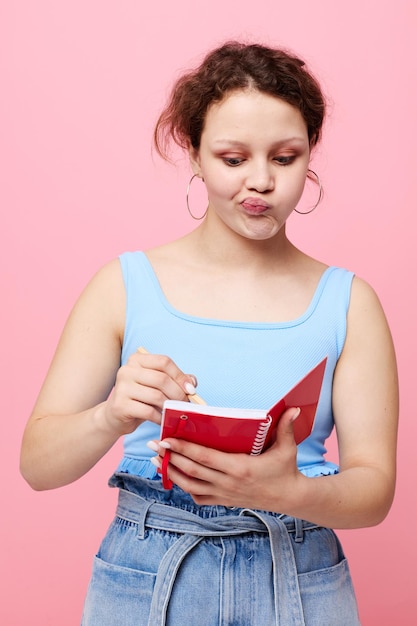 Jeune femme écrivant dans un cahier rouge avec un stylo étude fond de couleur rose inchangé