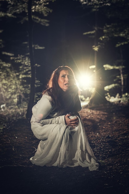 Jeune femme effrayée dans la forêt la nuit en robe blanche. Scène d'horreur.