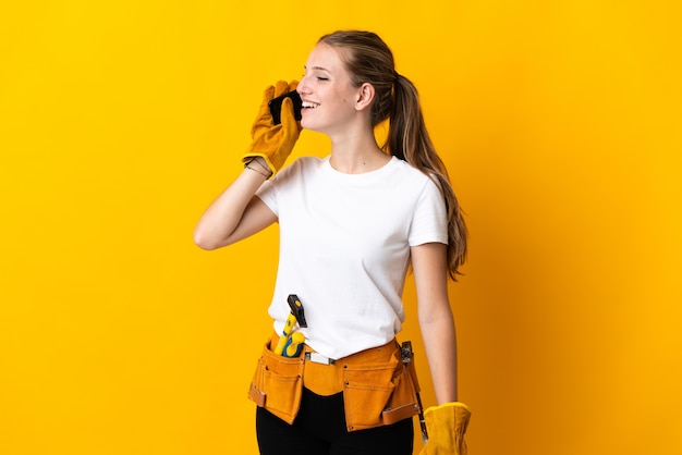 Jeune femme électricienne isolée sur fond jaune en gardant une conversation avec le téléphone mobile