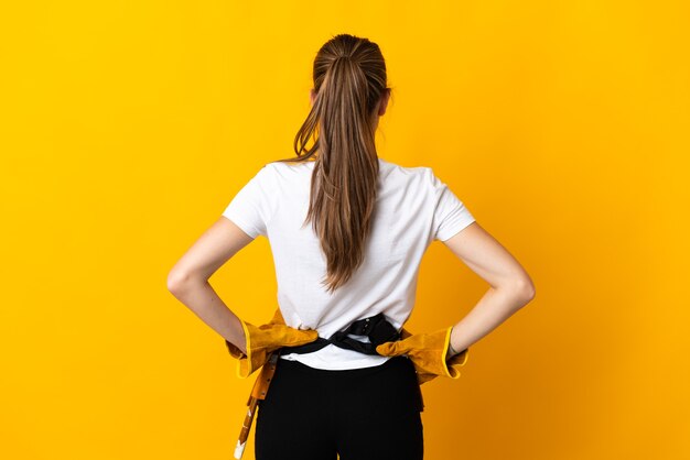 Jeune femme électricienne isolée sur mur jaune en position arrière