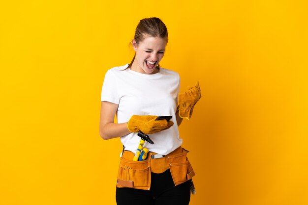 Jeune femme électricienne isolée sur mur jaune avec téléphone en position de victoire