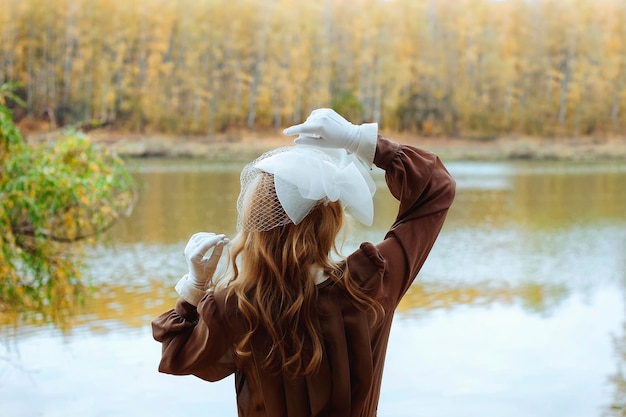 Jeune femme élégante assise en robe rétro et vêtements vintage et souriante dans le parc d'automne jaune.