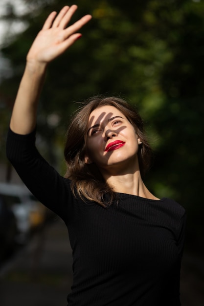 Une jeune femme élégante aux lèvres rouges couvre son visage des rayons du soleil