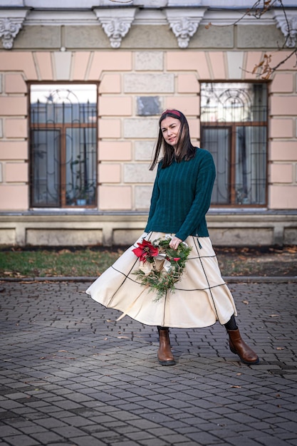 Jeune femme élégante avec une couronne de Noël à l'extérieur en attendant Noël