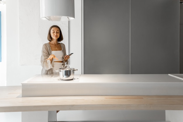 Jeune femme élégante cuisinant sur une plaque à induction dans une cuisine moderne. Concept de technologies intelligentes d'appareils de cuisine