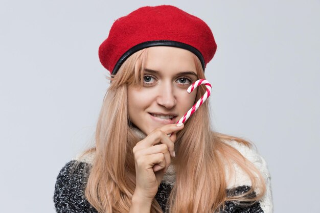 Photo une jeune femme élégante dans un béret rouge pose en jouant avec une canne à bonbons apportant une atmosphère festive