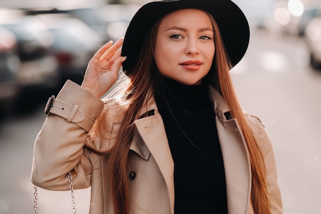 Jeune femme élégante dans un manteau beige dans un chapeau noir dans une rue de la ville. Mode de rue féminine. Vêtements d'automne. Style urbain.