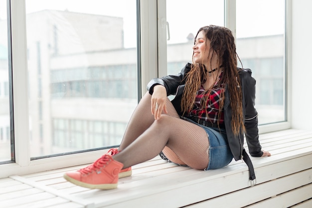 Jeune femme élégante avec des dreadlocks assis sur le rebord de la fenêtre