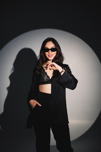 Jeune femme élégante et élégante dans un costume noir Studio shot Une femme dans un costume noir et des lunettes noires sur fond blanc