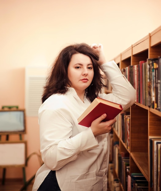 Jeune femme élégante lisant un livre dans la bibliothèque Mode décontractée look élégant Modèle grande taille