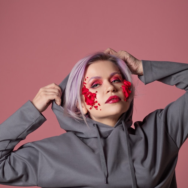 Jeune femme élégante et lumineuse avec le maquillage coloré et les pétales de fleur sur son visage