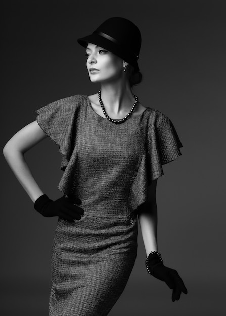 Jeune femme élégante, mode rétro, chapeau, gants, robe. Image en noir et blanc.