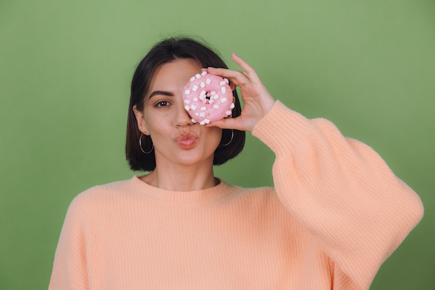 Jeune femme élégante en pull pêche décontracté isolé sur mur d'olive verte envoyer baiser avec espace copie beignet rose