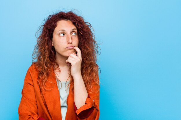 Jeune femme élégante rousse à la recherche de côté avec une expression douteuse et sceptique.