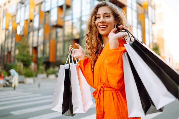 Une jeune femme élégante avec des sacs d'achat marchant dans une rue ensoleillée dans une robe lumineuse Concept de vente