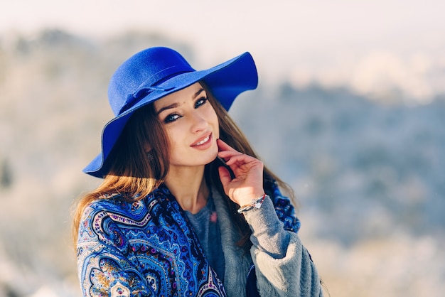 Jeune femme élégante souriante au chapeau bleu et foulard marchant dans le parc