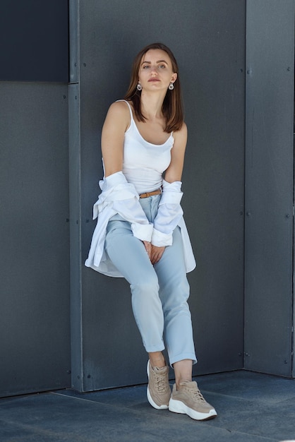 Photo une jeune femme élégante en tenue décontractée se tient près du mur gris du bâtiment moderne