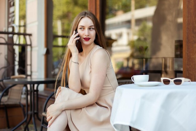 Une jeune femme élégante en train de parler au téléphone alors qu'elle est assise à une table dans un café.
