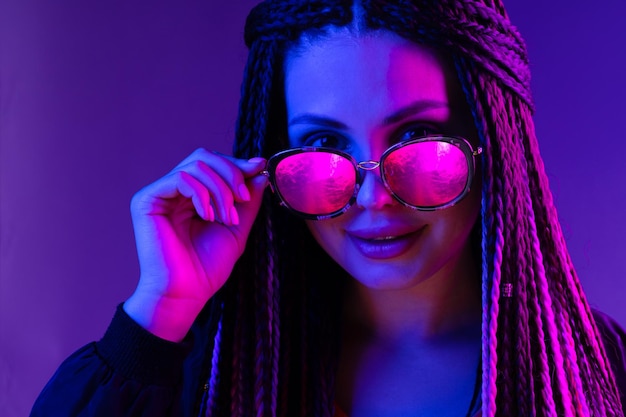 Jeune femme élégante avec des tresses portant des lunettes de soleil sur fond violet