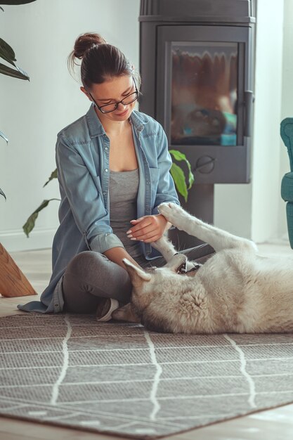 Jeune femme élevant et jouant avec son chien domestique husky sibérien à la maison