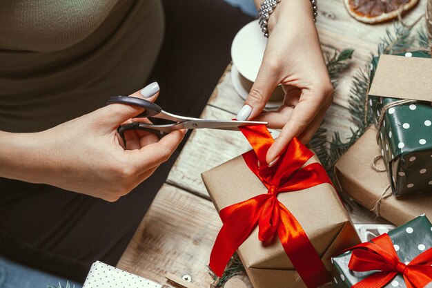 Jeune femme d'emballage et décore beaucoup de pile de cadeaux